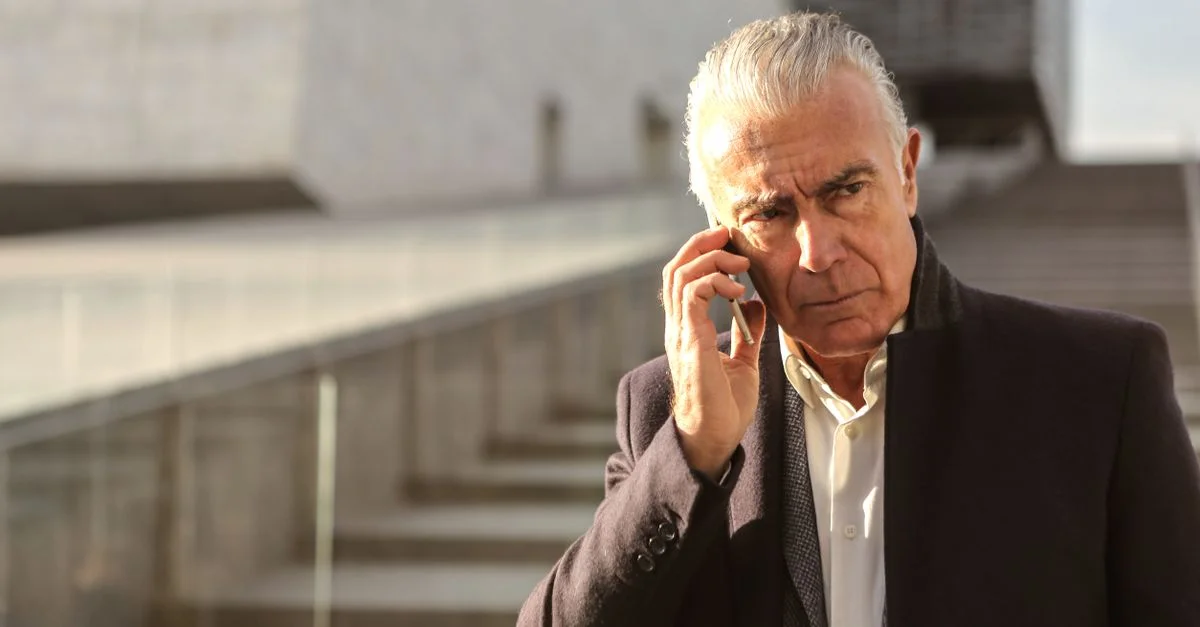 Homme d'affaires senior sérieux utilisant un smartphone à l'extérieur, dégageant une ambiance professionnelle et pensive.