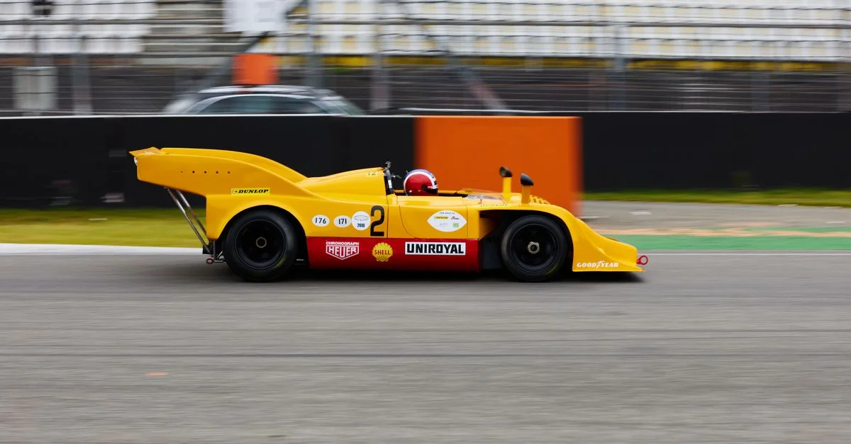 Voiture de course vintage jaune roulant à toute allure sur le circuit de Hockenheimring. Capture le mouvement et le design automobile.